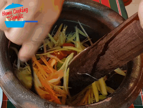 Using a spoon and pestle, the shredded papaya strips are thoroughly mixed in the mortar.