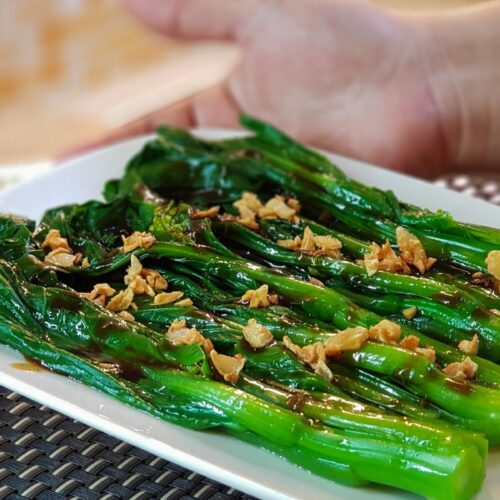 A pair of hands holding the finished choy sum dish.
