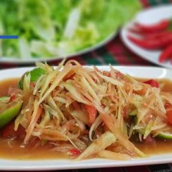 Green papaya salad on a white serving dish, with lettuce, chilli and lime in the background.