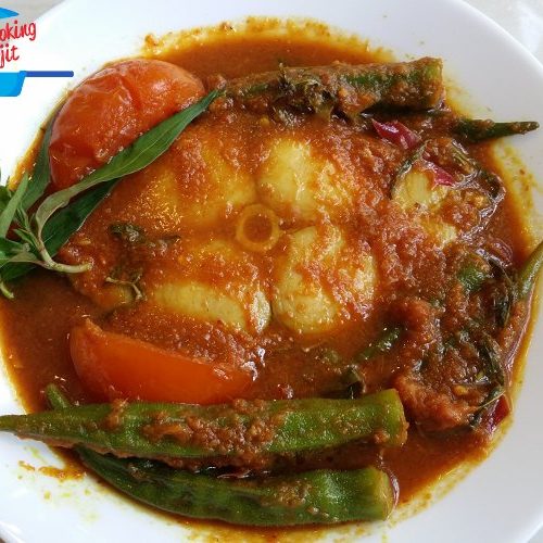 A slice of Narrow-Barred Spanish Mackerel, some okras and tomatoes, served with assam pedas curry gravy in a plate.